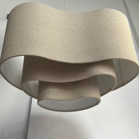 a natural linen 3 tiered lampshade in an unusual kidney shape in front of a white background