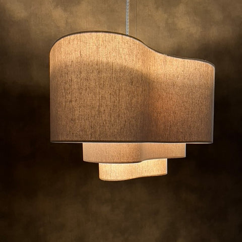 a beige 3 tiered lampshade in an unusual kidney shape in front of a textured background