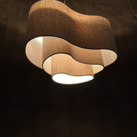 a beige lit  3 tiered lampshade in an unusual kidney shape from below in a dark setting