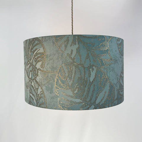 A sophisticated peacock blue drum lampshade made from luxurious jacquard fabric. Its frosted inner lining and beach gold frame add a touch of elegance to any room.