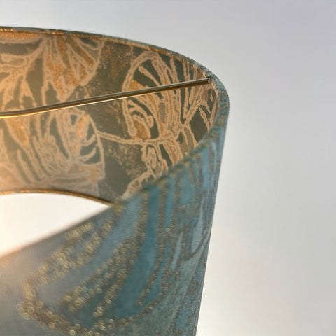 A stunning peacock blue jacquard lampshade with a frosted inner lining, enhanced by a sleek beach gold frame, perfect for adding a touch of class to any interior.