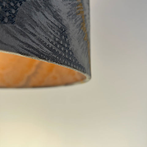 A sleek silver drum lampshade made from jacquard fabric, with a frosted clear inner lining. Its luxurious design adds a sophisticated element to any room.