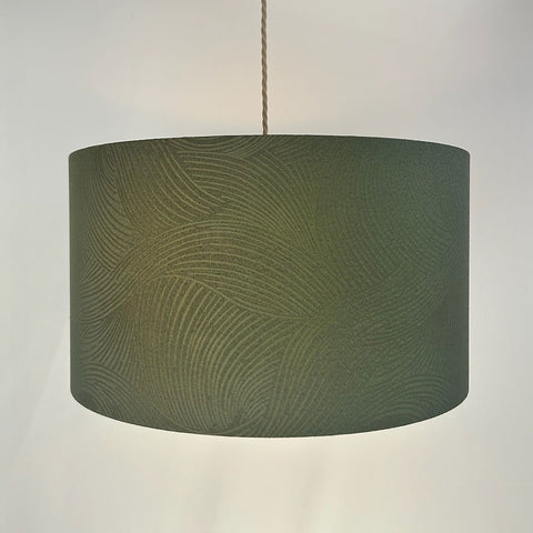 A sophisticated hand made drum lampshade crafted from dark moss green jacquard fabric. The frosted inner lining and beach gold frame provide a refined touch, perfect for adding elegance to any room.