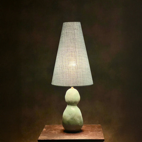 A table lamp with a blue conical shade and a green gourd-shaped base, placed on a wooden surface against a dark background.