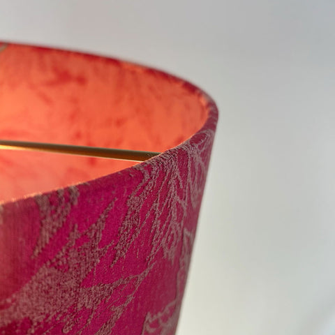 A close-up of a handmade lamp shade in a vibrant fuchsia red jacquard fabric with a delicate embroidered maple leaf pattern. This beautiful lampshade features a frosted clear inner lining and a sleek beach gold frame, designed to complement both contemporary and traditional interiors.