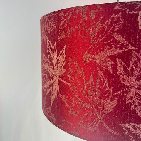 A vibrant fuchsia red drum lampshade in close-up with a delicate maple leaf pattern in a rich jacquard fabric. The sophisticated fabric will add a touch of modern elegance to any room. Available in various sizes, it is designed to complement both contemporary and traditional interiors