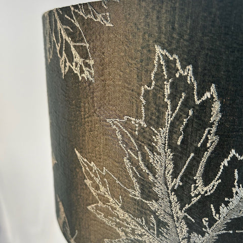 A close-up of a handmade green lampshade featuring intricate maple leaf embroidery in warm, fall colours. This elegant drum lampshade is designed to bring a touch luxury to any space.