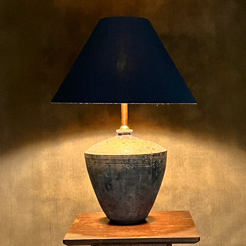 A table lamp with a blue conical lampshade, sitting on a wooden surface, with a textured blue-grey base.