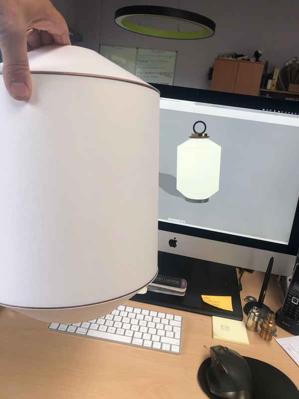 White lampshade being held over a desk setup with a computer monitor.