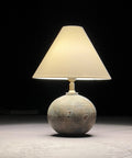 A table lamp with a stoneware base and a silk coolie lampshade, illuminated, set against a dark background.