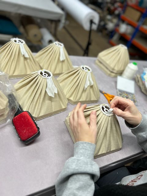 Person working on decorative lampshades with a red tool on a table.