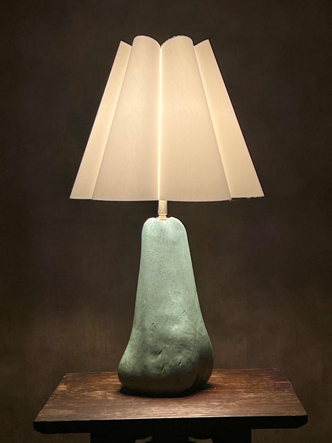 Table lamp with a textured green base and white pleated shade on a dark background